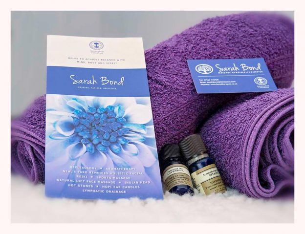 A stack of purple towels, two small amber essential-oil bottles and Sarah Bond's printed gift voucher